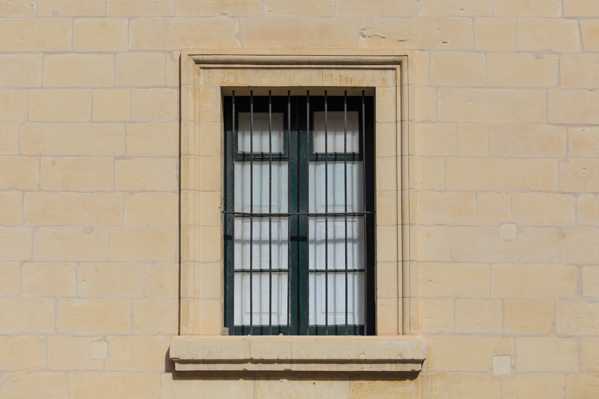 Malta, Valletta. Facade of yellow limestone house with closed window with metal bars